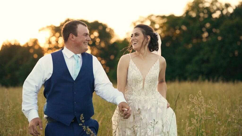 Bride and groom walking hand in hand through a field during golden hour at a Missouri wedding