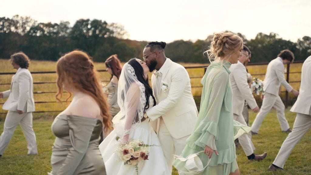 Bride and groom kissing as their wedding party walks past at a Missouri outdoor wedding.